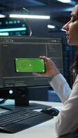 Vertical Zoom in on green screen mobile phone used by data center employee troubleshooting issues. Engineer uses mockup smartphone device in server hub, establishing performance benchmarks, camera B video