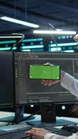 Vertical Technician using mockup mobile phone in data center, managing servers. Expert in server hub using isolated screen smartphone to ensure networks are secure and functioning properly, camera B video