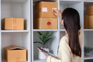 Young Woman Checking Online Product Orders on Tablet in Modern Home Office with Shelves of Boxes photo