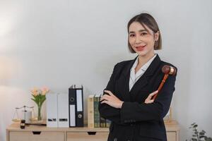 Confident Young Lawyer in Professional Office Setting Holding Gavel with Books and Legal Documents in Background photo