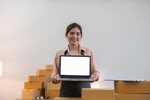 Woman Entrepreneur Selling Products Online from Home Office with Boxes of Inventory and Laptop photo