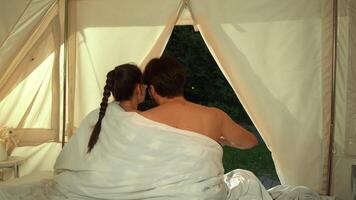 Couple in love is sitting on the bed, under a blanket, enjoying the view from the tent. Medium shot. Slow motion. video