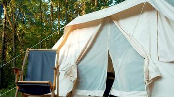 Woman steps out of a tent in the forest campground and sits down on a comfortable chaise longue. video