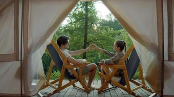 Couple of tourists, sitting in front of their tent, make a heart with their hands and smile for the camera. video