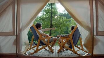 Couple in love are relaxing in nature. They are sitting in front of their tent, enjoying a beautiful view of the forest. video