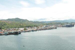An aerial view of boats docked in a harbor surrounded by lush green hills and a blue sky with clouds. photo