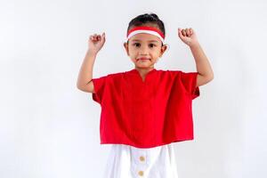 A joyful little Asian girl with a red and white ribbon on her head posing with both hands raised as if holding something. Indonesian Independence day concept. photo