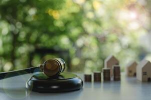 A gavel sits on a wooden surface with a stack of coins and a house model. The scene suggests a courtroom setting, with the gavel symbolizing authority and the coins photo