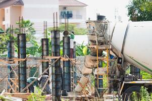 A cement mixer is pouring concrete into a building. The workers are wearing hard hats and safety gear. The scene is busy and active, with people working on the construction site photo