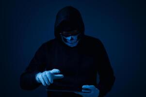 A hacker with a tablet, a criminal in the dark, uses advanced technology to spy and steal data, posing a serious security threat as a modern-day tech-savvy thief. photo