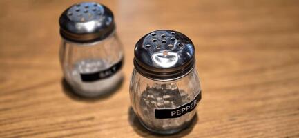 simple American diner style salt and pepper glass shakers sits on table with wooden background, selective focus background, good for recipe book or web blog photo