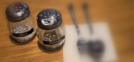 simple American diner style salt and pepper glass shakers sits on table with wooden background, selective focus background, good for recipe book or web blog photo