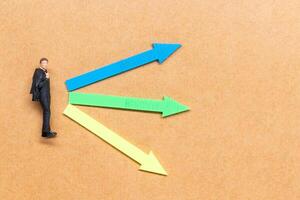 A miniature people stands at the intersection of colorful arrows on a light brown background photo