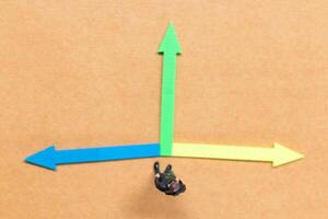 A miniature people stands at the intersection of colorful arrows on a light brown background photo