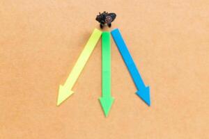 A miniature people stands at the intersection of colorful arrows on a light brown background photo