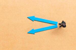 A miniature people stands at the intersection of colorful arrows on a light brown background photo