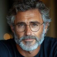 A middle-aged man with a beard and glasses smiles warmly in soft evening lighting photo