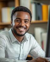 A young man smiles confidently while using a computer in a bright office space photo