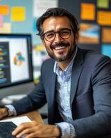 A cheerful man in a suit smiling at his computer in a vibrant office environment photo