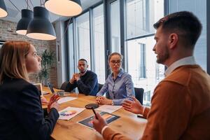 In the vibrant ambiance of a modern startup office, a diverse team of business professionals engage in discussions on various projects and develop new business strategies, epitomizing creativity and photo