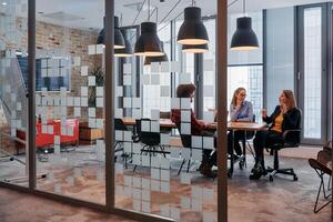 In the dynamic hustle and bustle of a business environment, a group of young business professionals walk down the corridor next to their office, while their colleagues collaborate inside, symbolizing photo