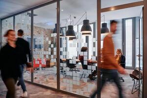 In the dynamic hustle and bustle of a business environment, a group of young business professionals walk down the corridor next to their office, while their colleagues collaborate inside, symbolizing photo