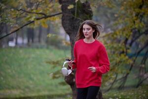 Young beautiful woman running in autumn park and listening to music with headphones on smartphone photo