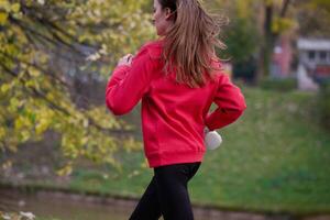 Young beautiful woman running in autumn park and listening to music with headphones on smartphone photo