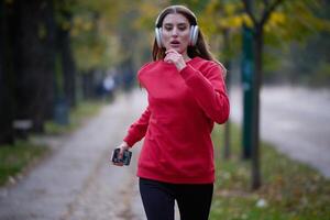 Young beautiful woman running in autumn park and listening to music with headphones on smartphone photo