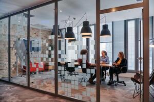 In the dynamic hustle and bustle of a business environment, a group of young business professionals walk down the corridor next to their office, while their colleagues collaborate inside, symbolizing photo