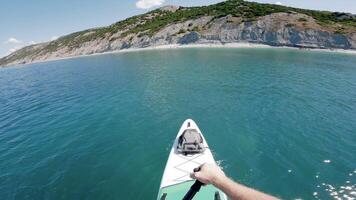 Men rowing on SUP board on transparent sea. First person view of stand paddle boarding in summer. video