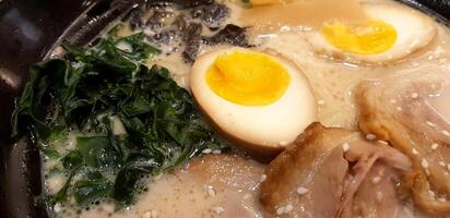 Close up Ramen noodle with seaweed, slices of pork and two half boiled eggs in hot miso soup at restaurant. Delicious Japanese food concept and Selective focus on egg. photo
