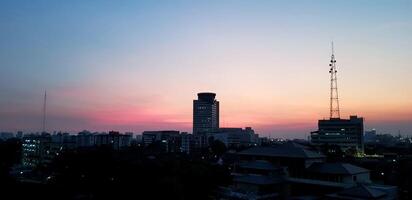Building and telecommunication tower with sunset or sunrise time and clouds. Cityscape view and silhouette structure concept photo