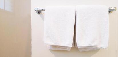 Two white clean towel and napkin hanging on stainless hanger with white wall background for customer using in bathroom with copy space. Cleaning, Shape and Surface of stone concept. photo