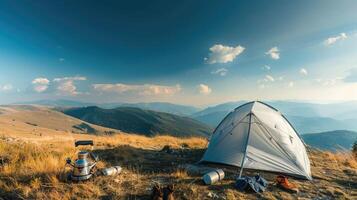 Big white camping tent on grassy hilltop, camping gear scattered around, panoramic view of mountains under clear blue sky. Big camping tent gears photo