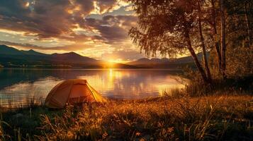 Serene camping scene during golden hour with tent by calm lake, sun setting behind mountains, sky filled with golden hues, peaceful and idyllic atmosphere. Camping taken during golden hour photo