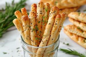 Selection of breadsticks with sesame seeds and herbs, displayed in a tall glass jar photo