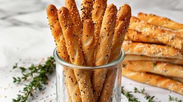 Selection of breadsticks with sesame seeds and herbs, displayed in a tall glass jar photo
