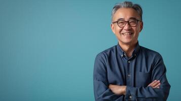 Smiling MiddleAged East Asian Man in Glasses with Arms Crossed against Blue Background for Professional Design photo