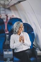 An attractive, elegant Asian businesswoman is sipping coffee while looking at the view outside the plane window, traveling on a business trip. businesspeople, transportation, luxurious lifestyle photo