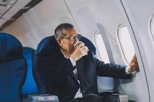 Attractive Asian male passenger of airplane sitting in comfortable seat while working laptop and tablet with mock up area using wireless connection. Travel in style, work with grace. photo