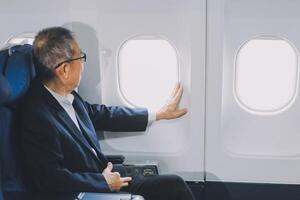 Attractive Asian male passenger of airplane sitting in comfortable seat while working laptop and tablet with mock up area using wireless connection. Travel in style, work with grace. photo