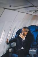 Attractive Asian male passenger of airplane sitting in comfortable seat while working laptop and tablet with mock up area using wireless connection. Travel in style, work with grace. photo