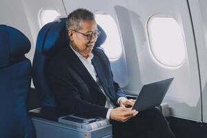 Attractive Asian male passenger of airplane sitting in comfortable seat while working laptop and tablet with mock up area using wireless connection. Travel in style, work with grace. photo