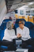 A mature couple enjoys a plane ride sitting near the window. They looked out into the sky. Immerse yourself in the scenery and excitement of the journey. To create precious memories together photo