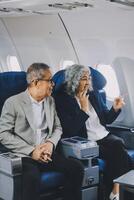 A mature couple enjoys a plane ride sitting near the window. They looked out into the sky. Immerse yourself in the scenery and excitement of the journey. To create precious memories together photo