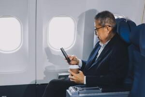 Attractive Asian male passenger of airplane sitting in comfortable seat while working laptop and tablet with mock up area using wireless connection. Travel in style, work with grace. photo