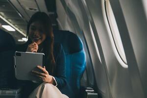 Young Asian executive excels in first class, multitasking with digital tablet, laptop and smartphone. Travel in style, work with grace. photo