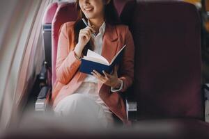 Attractive Asian female passenger of airplane sitting in comfortable seat while working laptop and tablet with mock up area using wireless connection. Travel in style, work with grace. photo