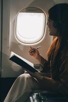 A young Asian woman, seated as an airplane passenger, contemplates dollar bills, reflecting on lucrative opportunities and aspirations towards billionaire status. photo